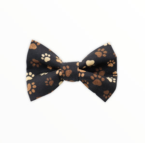 Handmade dog bow tie in cotton print. Made by hand in the U.K. and washable. Black cotton poplin covered in muddy brown paw prints.