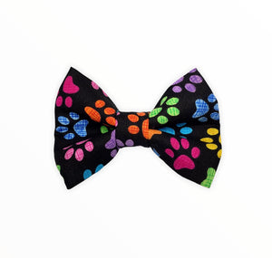 Handmade dog bow tie in cotton print. Made by hand in the U.K. and washable. Black poplin cotton printed with rainbow paw prints. 